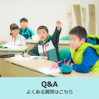 教材を開いて席についている4人の子どもの内、中央に座る男の子が手をあげている写真（Q&Aのページへリンク）