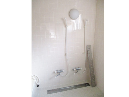 綺麗な白いタイル一面に丸い照明と蛇口がついたシャワーヘッド2つが設置されているシャワー室の写真