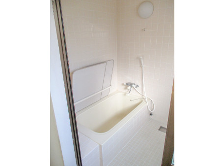 白いタイル一面に丸い形の照明があり、白い浴槽と立てかけられた浴槽の蓋とシャワーと蛇口がついている浴室内の写真