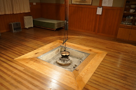 木のフローリングが光を反射しその中央に正方形の囲炉裏がある写真