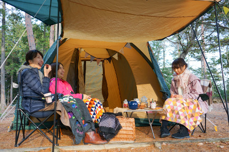 テントの外、タープの下でテーブルを囲み3人の女性が談笑している写真