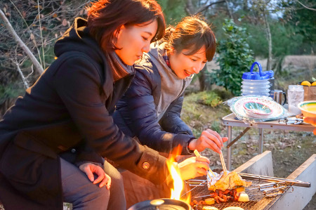 2人の女性が並んで、バーベキューコンロで焼いた物を箸で食べている様子の写真