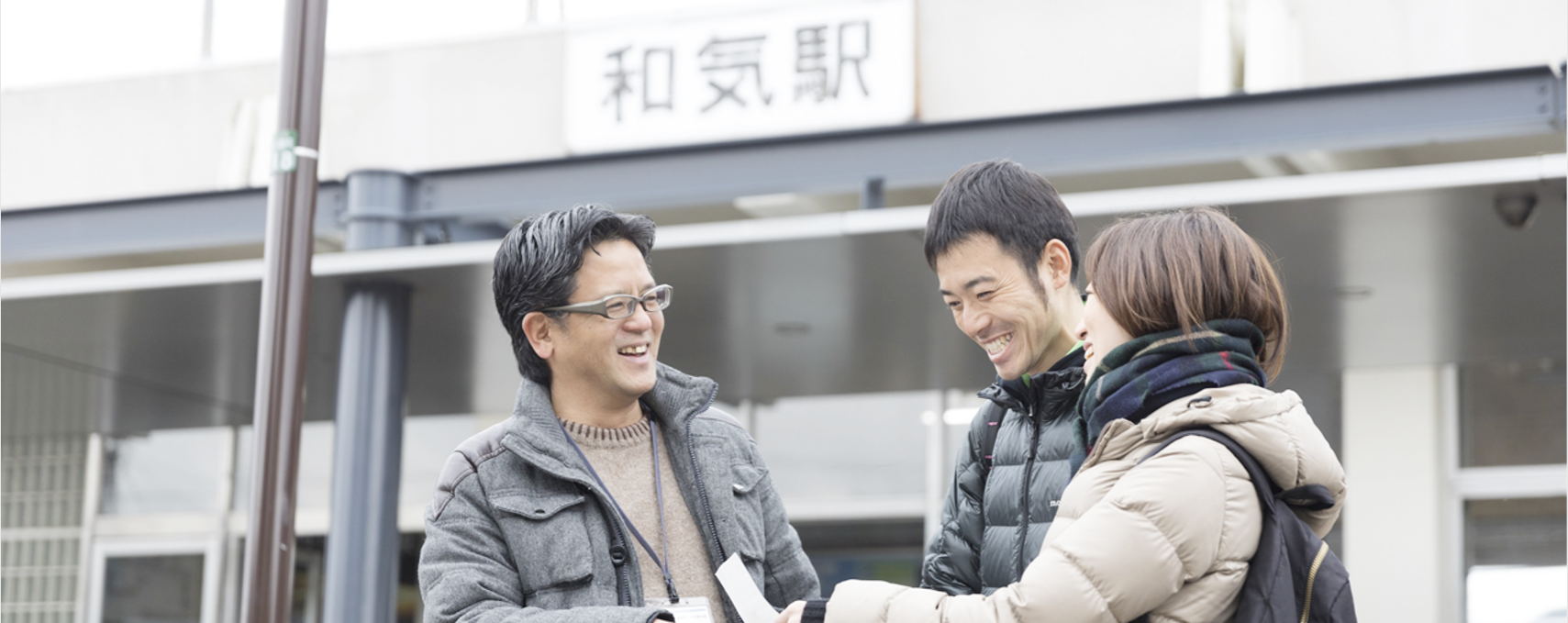和気駅の駅舎の前で、男性と女性が男性担当者と笑顔で話をしている写真