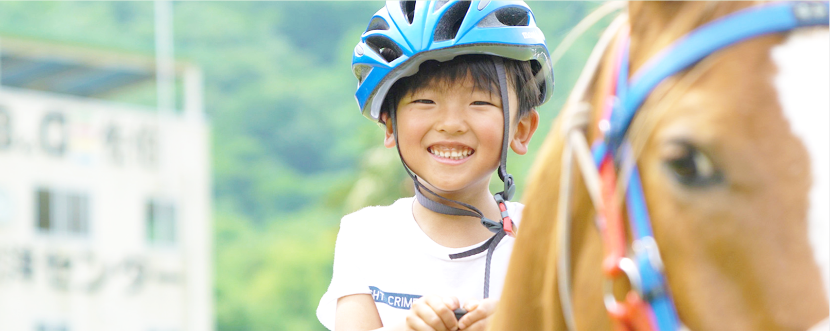 青色のヘルメットを被った男の子が乗馬しながら笑顔で正面を見ている写真