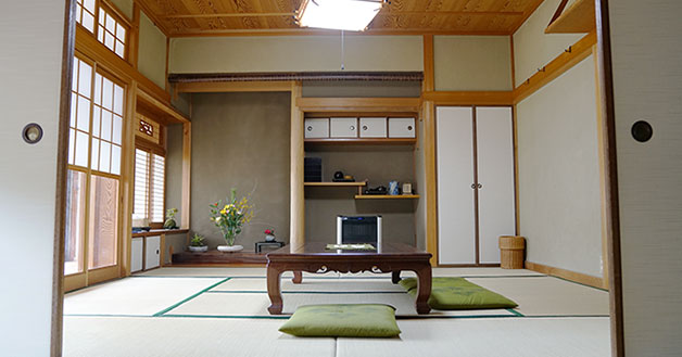 床の間のある畳敷きの和室の部屋中央に、大きなテーブルと緑色の座布団が設置された静耕舎の客室の写真