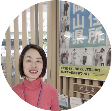 岡山県のパンフレットが並んでいるコーナーの前に立っている、大阪ふるさと暮らし情報センター岡山担当の佐藤さんの写真